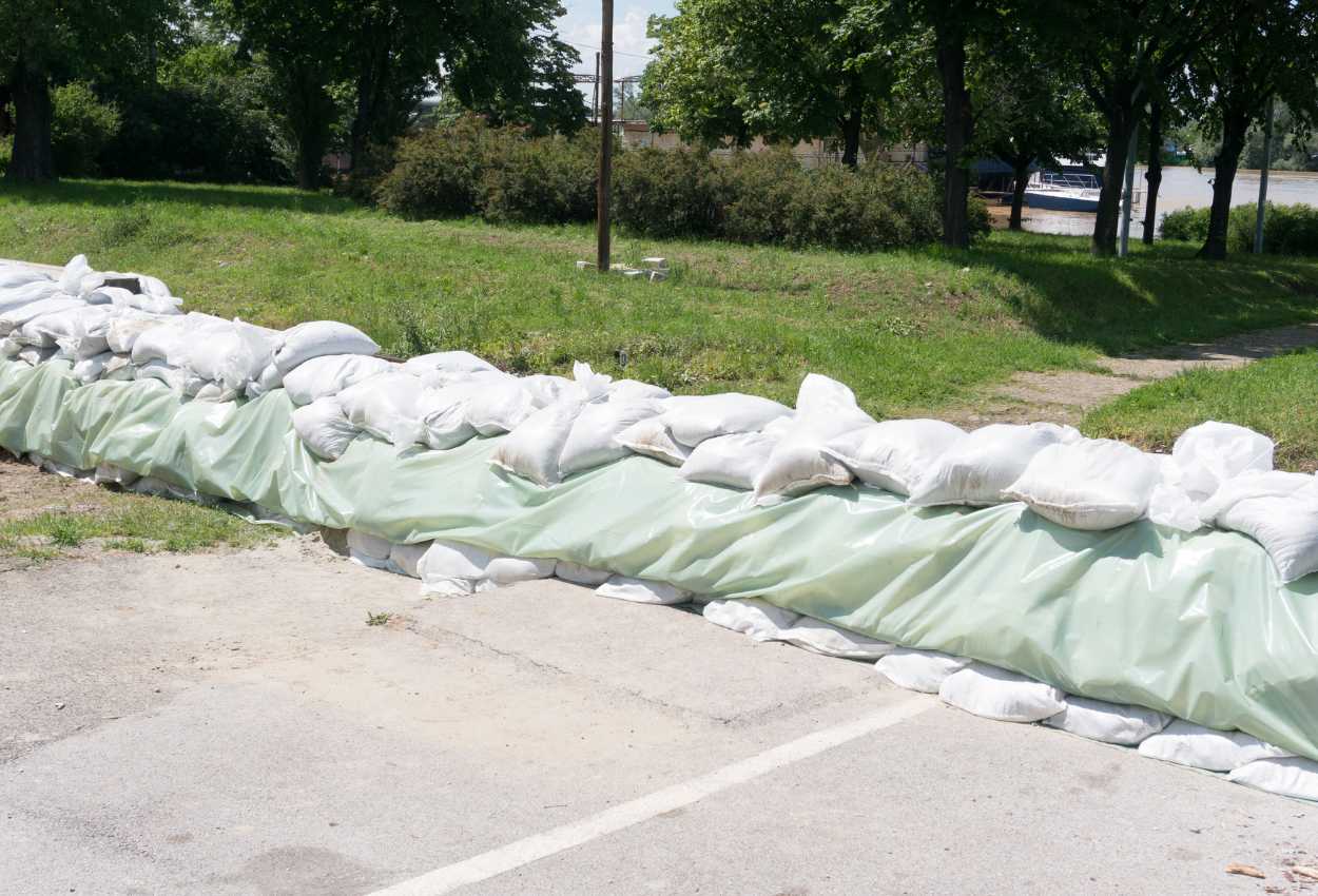 Barrière anti inondation composée de sacs de sable et renforcée par une bâche en plastique, installée pour protéger une zone riveraine.