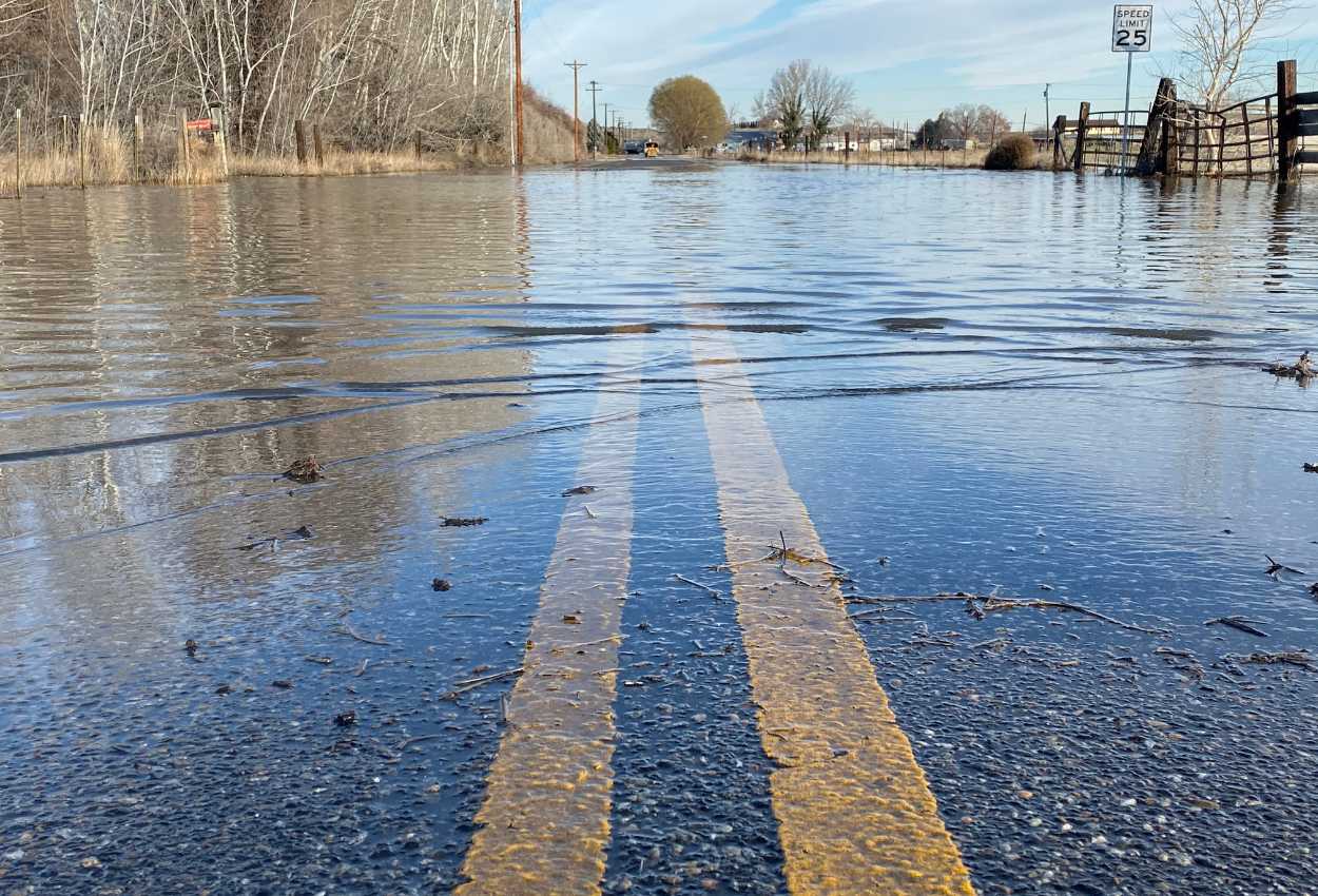 Une route inondée avec les lignes jaunes encore visibles sous l'eau, illustrant l'impact d'une crue sur l'infrastructure routière.